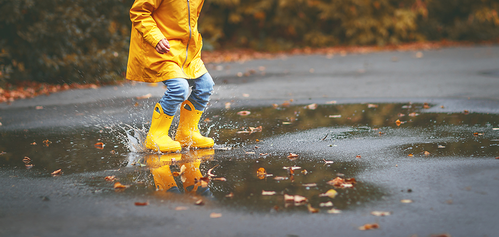 Legs of a child wearing yellow gumboots splashing in a puddle in autumn